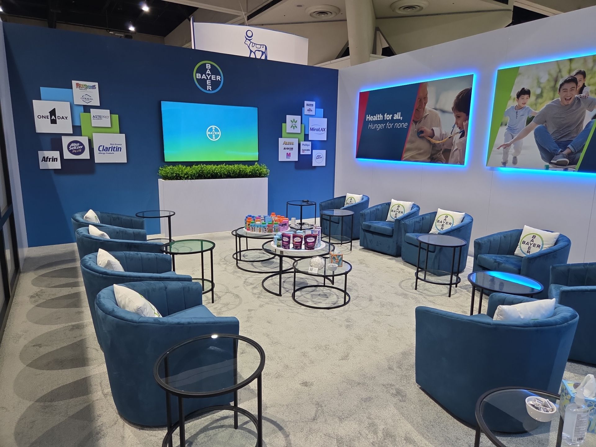 Booth interior — lounge seating area with brand logo wall, digital screen, and product displays